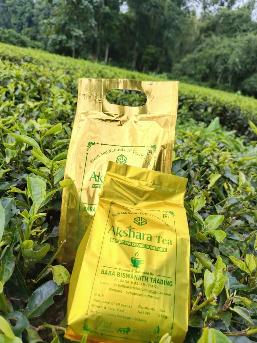 Akshara Tea 500 g and 250 g packs standing among tea bushes in Assam